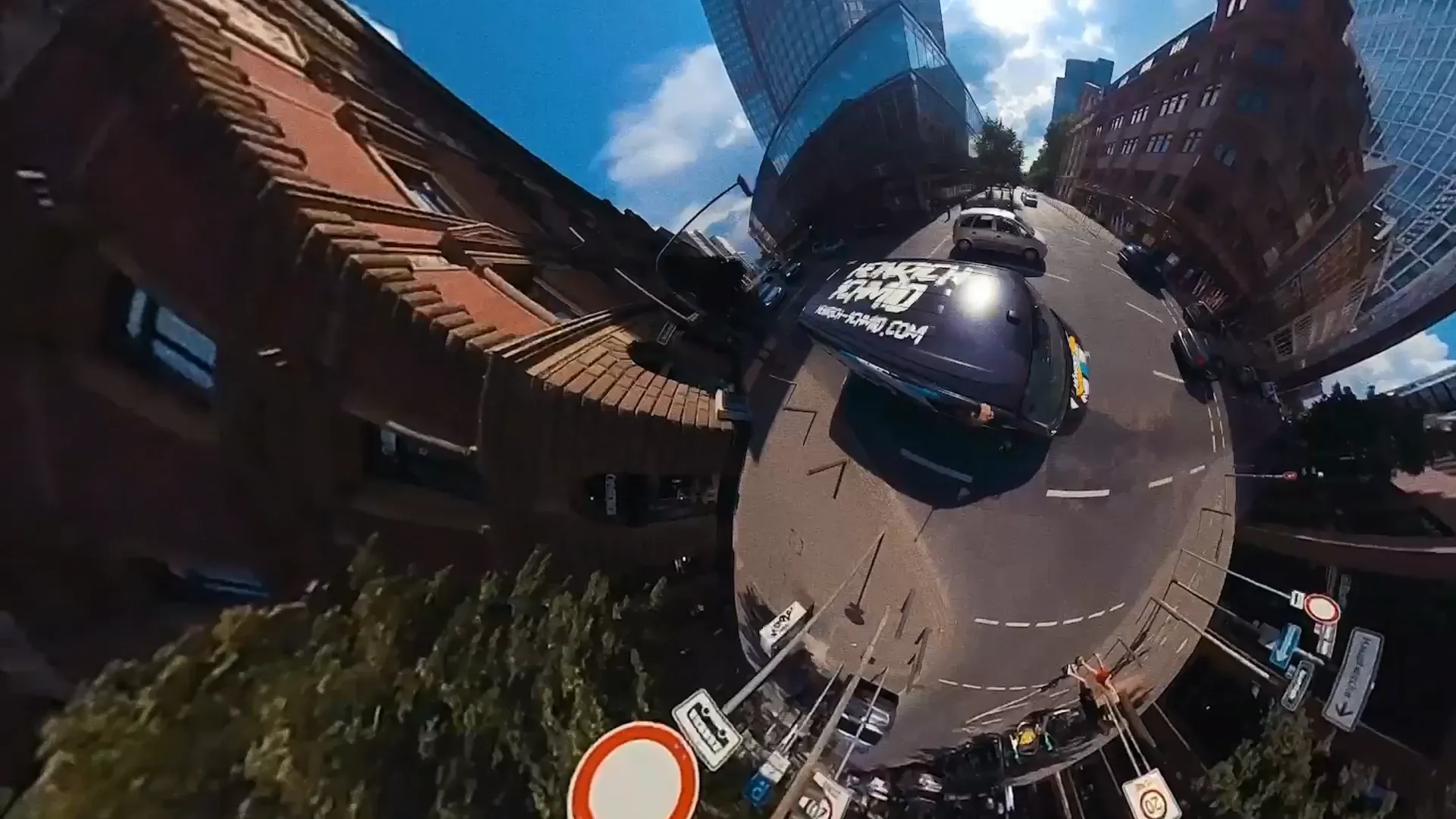 Tiny-Planet-Ansicht einer Stadtstraße mit schwarzem Fahrzeug, Hochhäusern und Verkehrsschildern