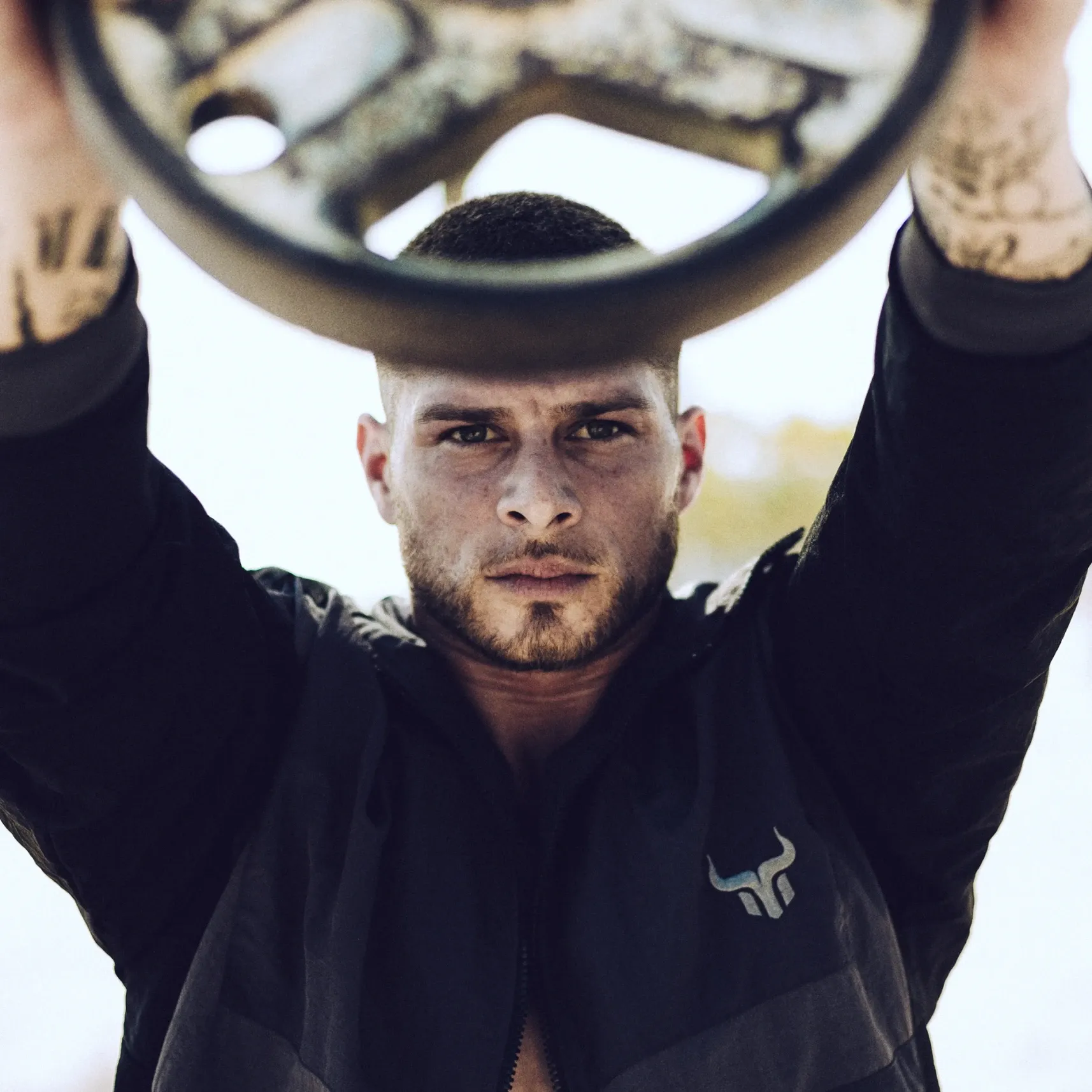 Sportler hält eine Hantelscheibe mit ausgestreckten Armen, fokussierter Blick