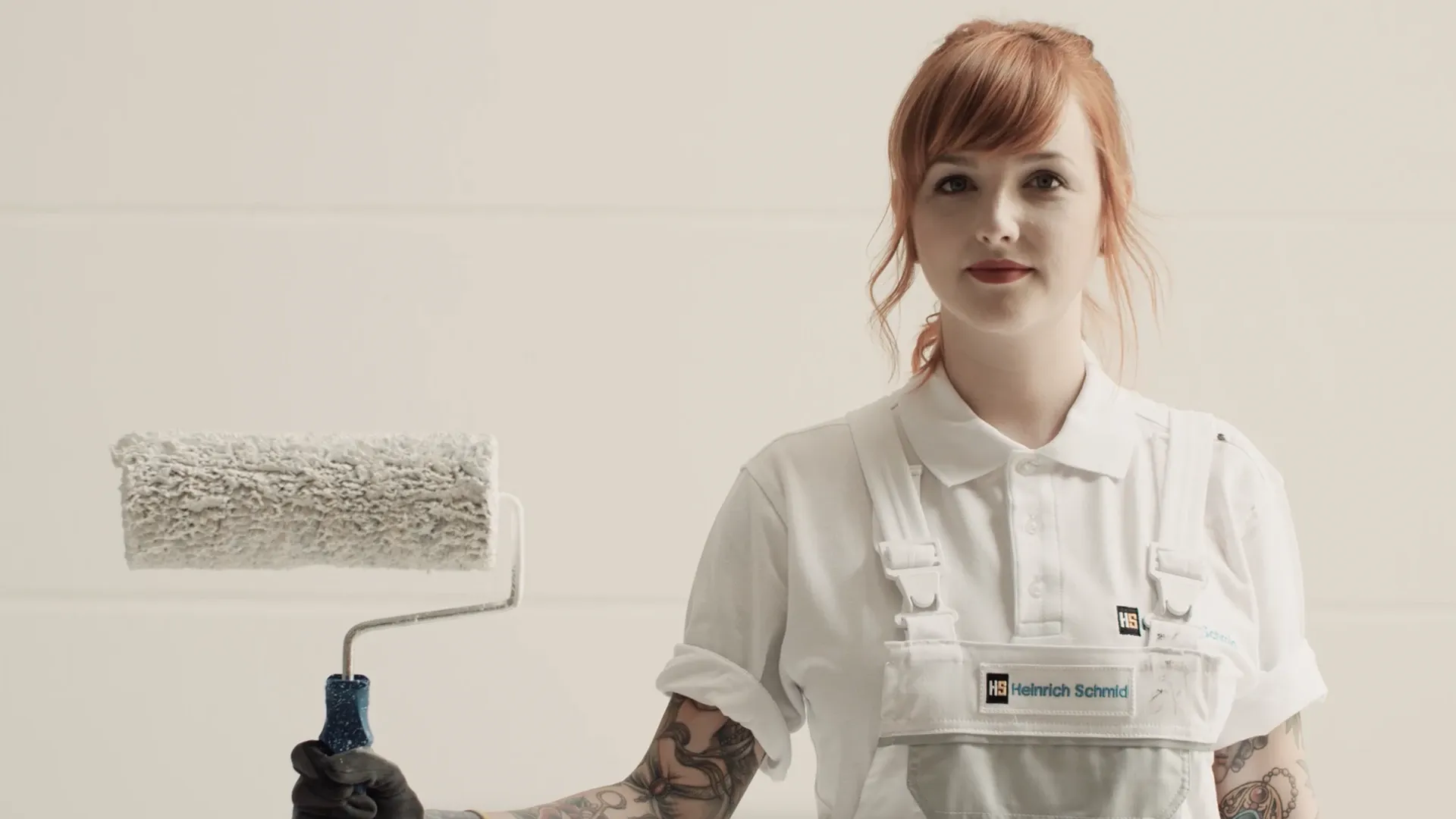 Person in weißer Maler-Arbeitskleidung mit Farbroller, Logo Heinrich Schmid auf der Latzhose