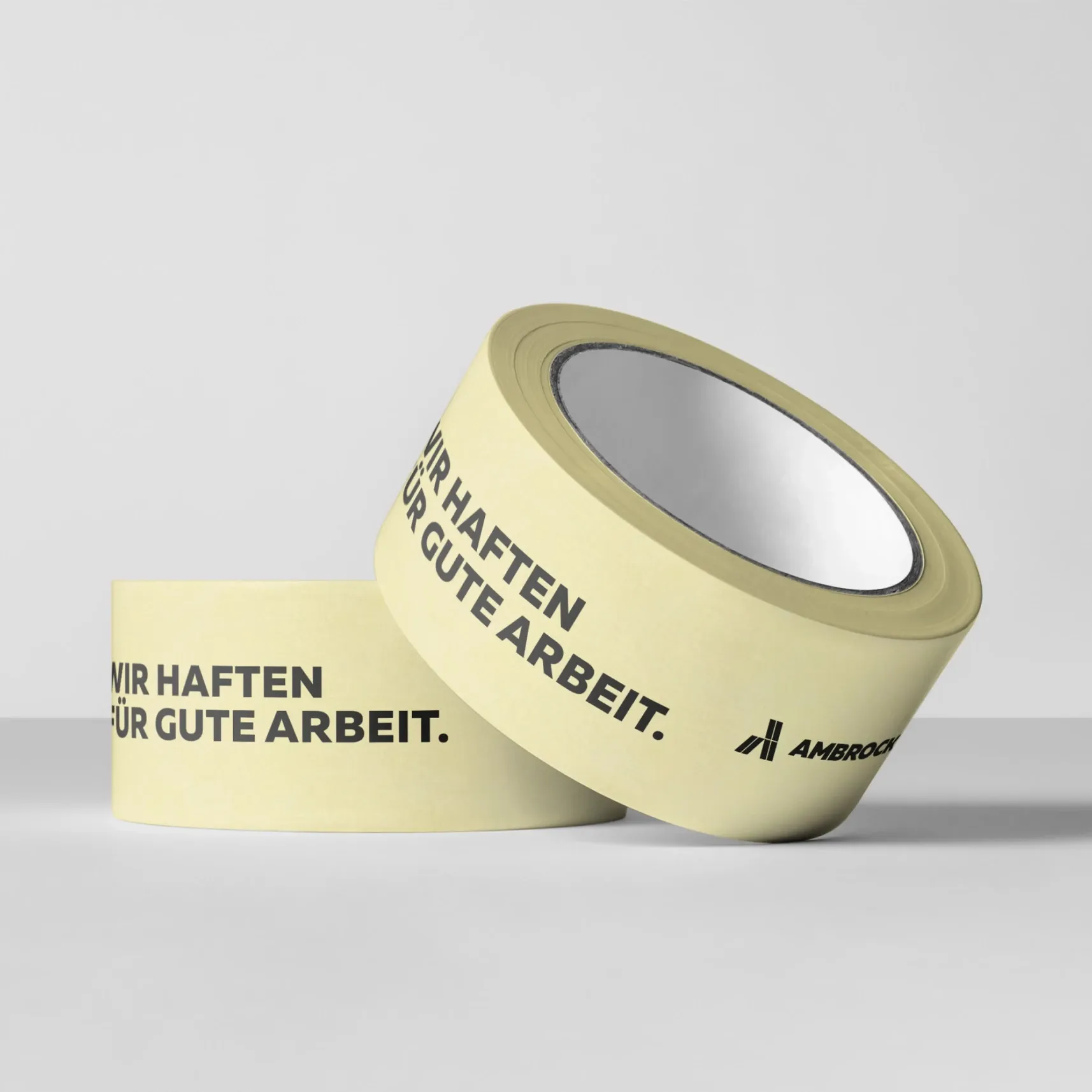 Zwei beige Klebebandrollen mit der Aufschrift „WIR HAFTEN FÜR GUTE ARBEIT“ auf neutralem Hintergrund