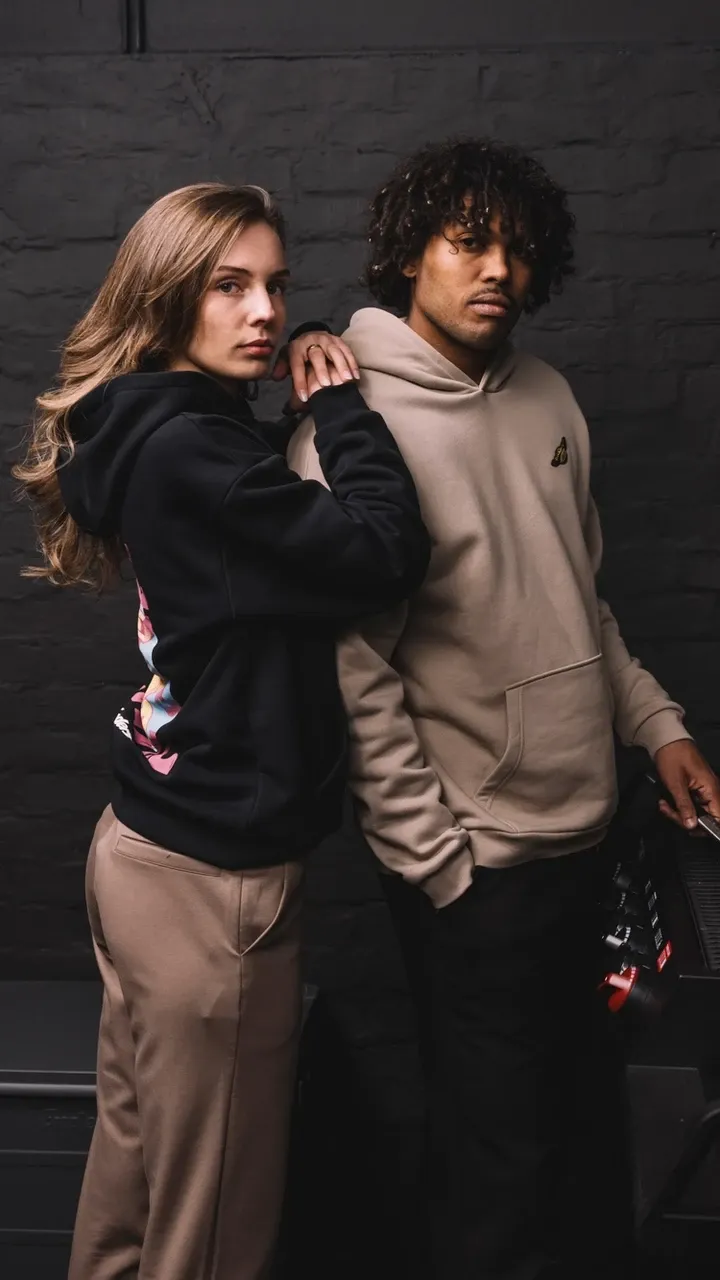 Zwei Personen in Hoodies an einem Gasgrill mit Burgern vor dunkler Wand