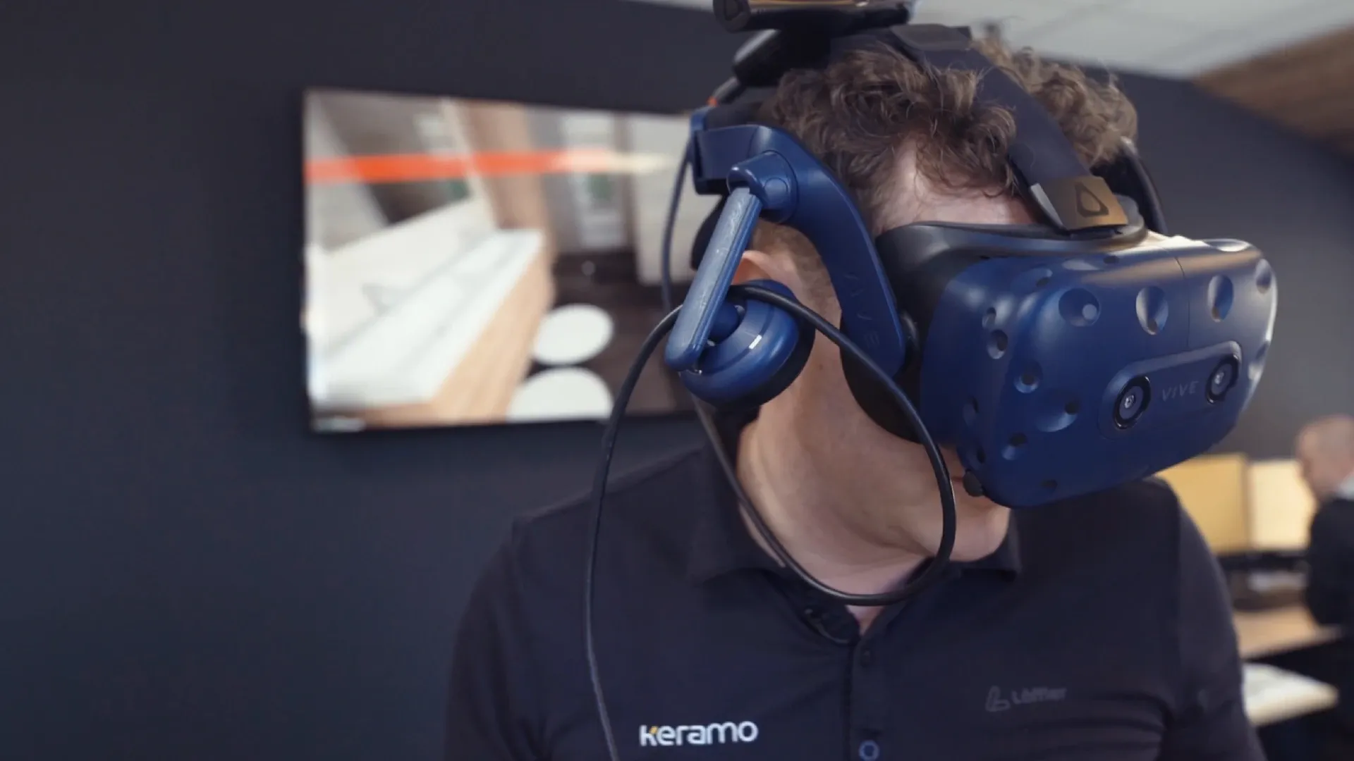 Person mit blauer VR-Brille in einem Büro, Bildschirm im Hintergrund