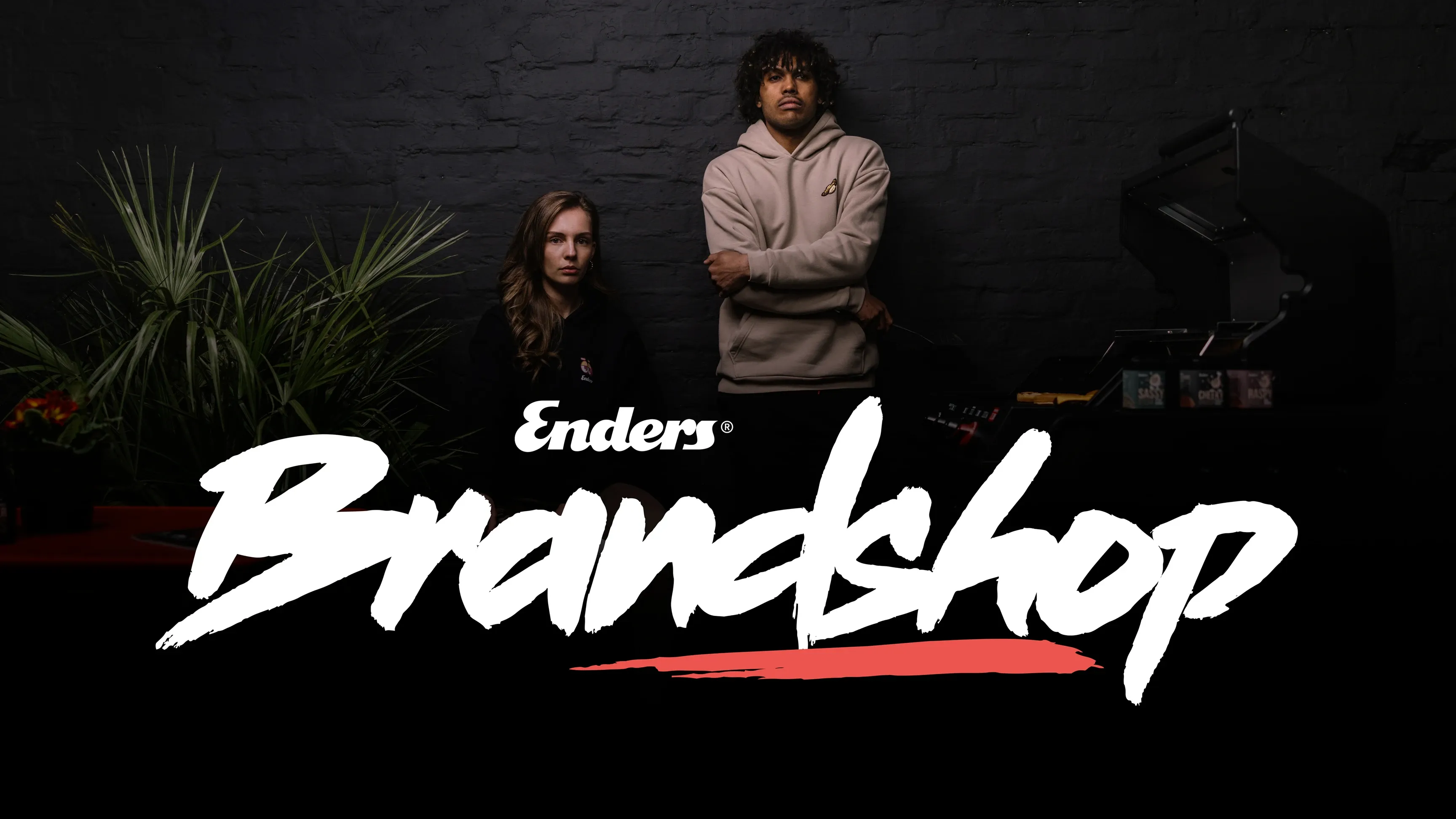 Zwei Personen vor dunkler Wand, Schriftzug 'Enders Brandshop', rechts ein Grill