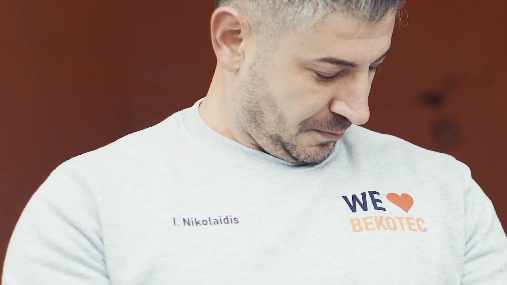 Person in grauem Sweatshirt mit Aufdruck „WE ♥ BEKOTEC“, schaut nach unten