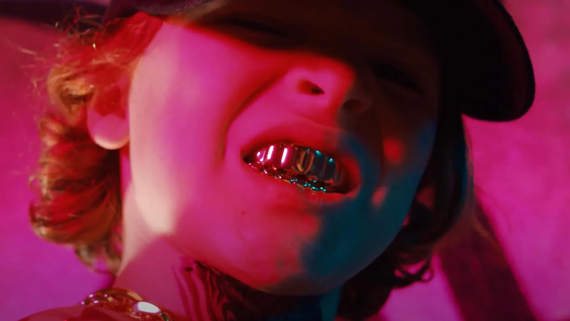 Nahaufnahme einer Person mit Basecap und metallischen Grillz im roten Neonlicht