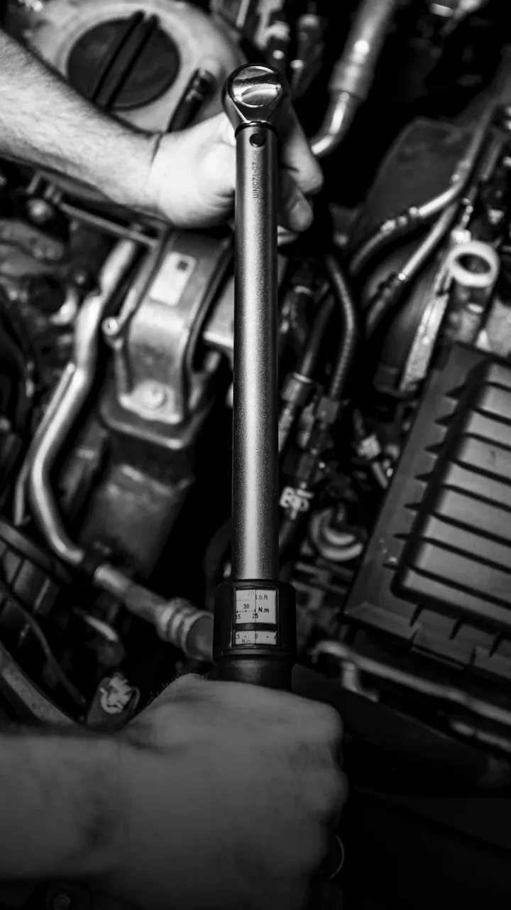 Hand mit Drehmomentschlüssel im Motorraum eines Autos