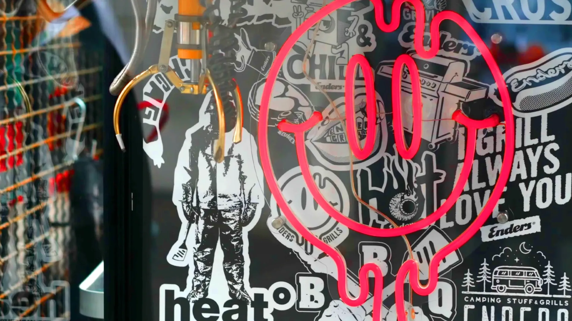 Pinkes Neon-Smiley vor einer Sticker-Collage mit BBQ-Motiven und hängenden Haken