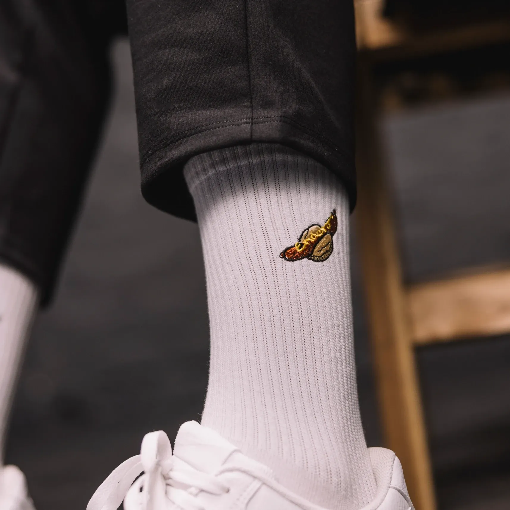 Weißer Sneaker und weiße gerippte Socke mit kleiner Stickerei, zu schwarzer Hose