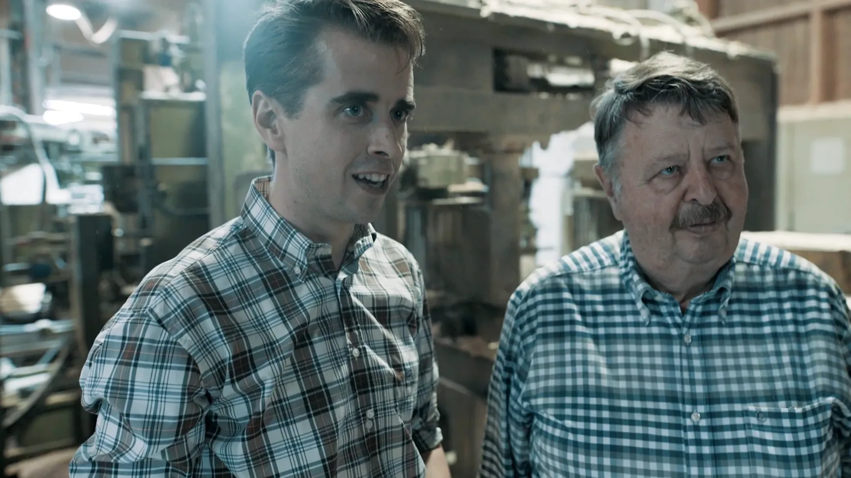 Zwei Männer in karierten Hemden stehen in einer Werkhalle und unterhalten sich.