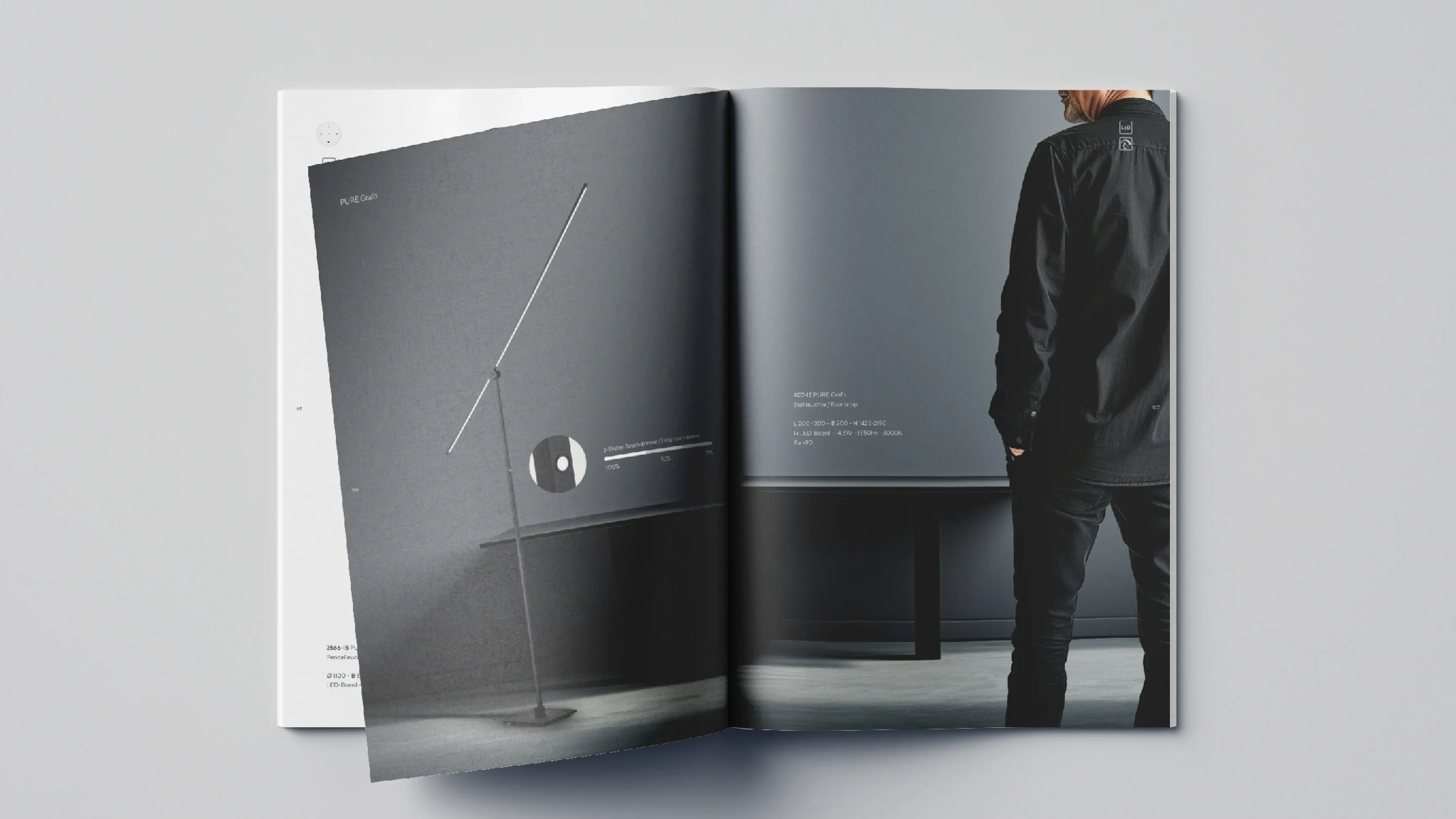 Aufgeschlagenes Magazin; links eine schlanke Stehleuchte, rechts eine schwarz gekleidete Person in grauem Raum