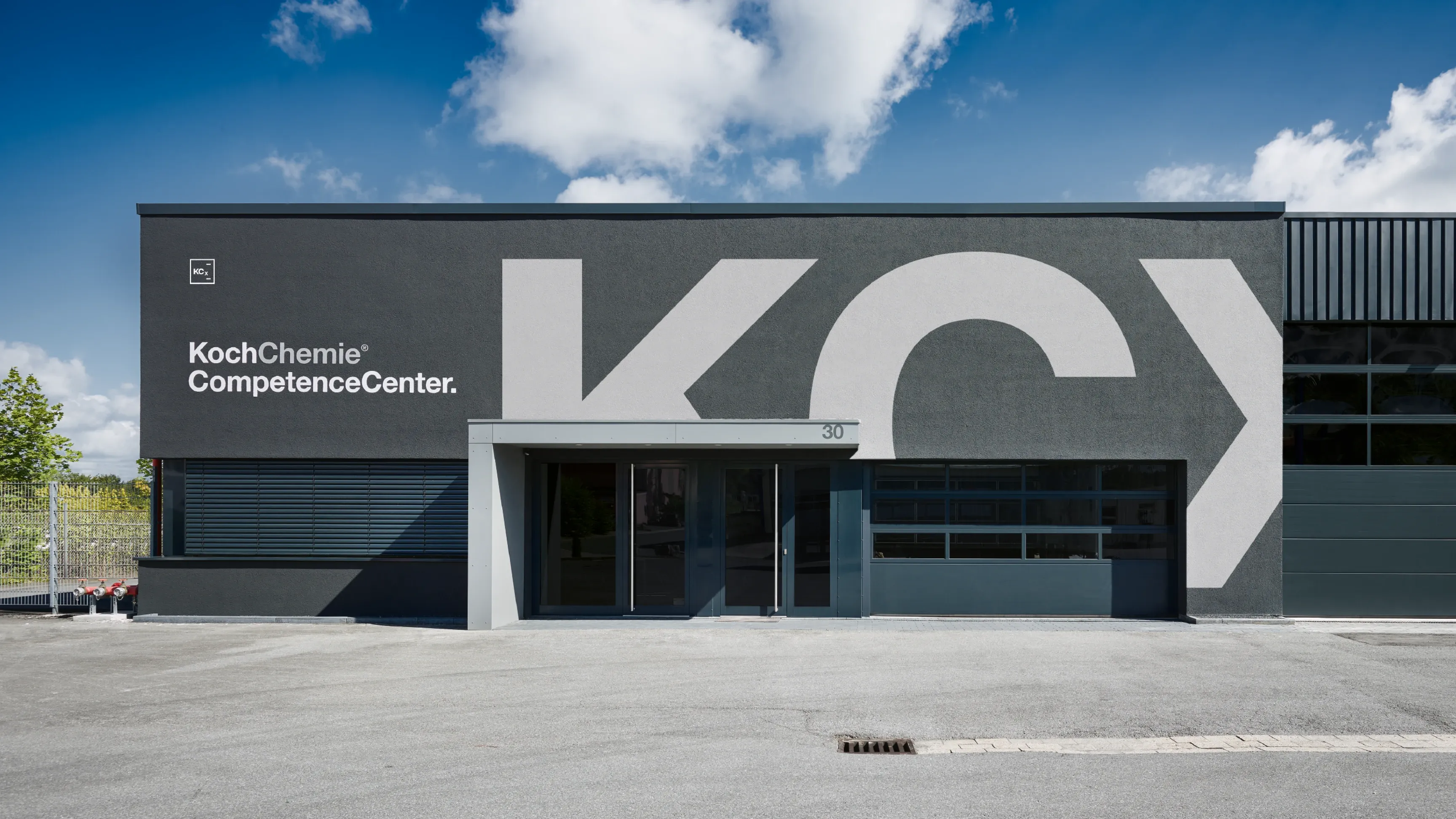 Graue Firmenfassade mit großer KC-Beschriftung und dem Schriftzug 'KochChemie CompetenceCenter' am Eingang