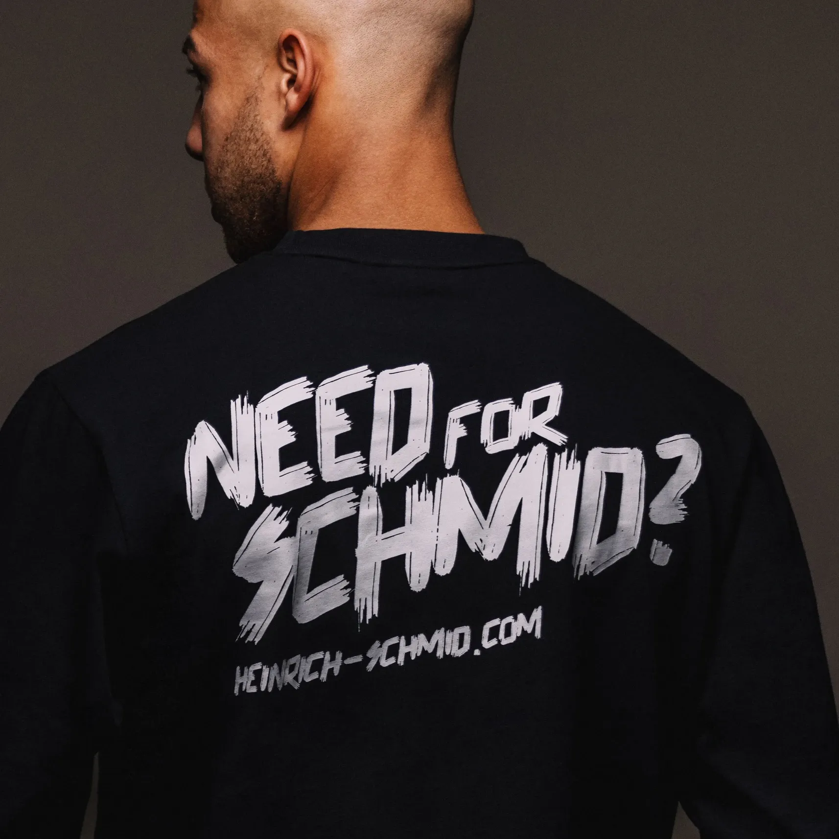 Rückansicht einer Person im schwarzen Shirt mit Aufdruck 'NEED FOR SCHMID?' und 'heinrich-schmid.com'