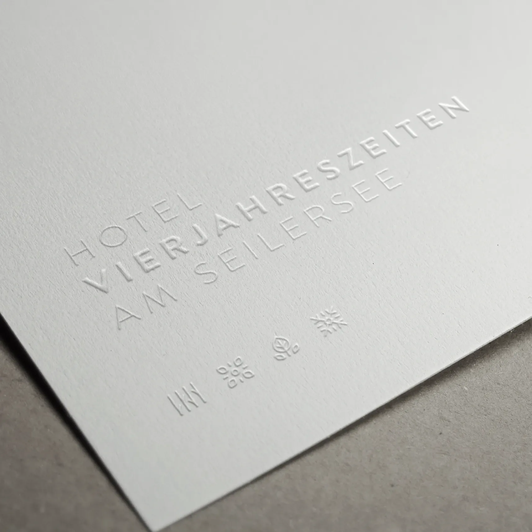 Geprägter weißer Karton mit Schriftzug „Hotel VIERJAHRESZEITEN AM SEILERSEE“ und kleinen Saison-Symbolen