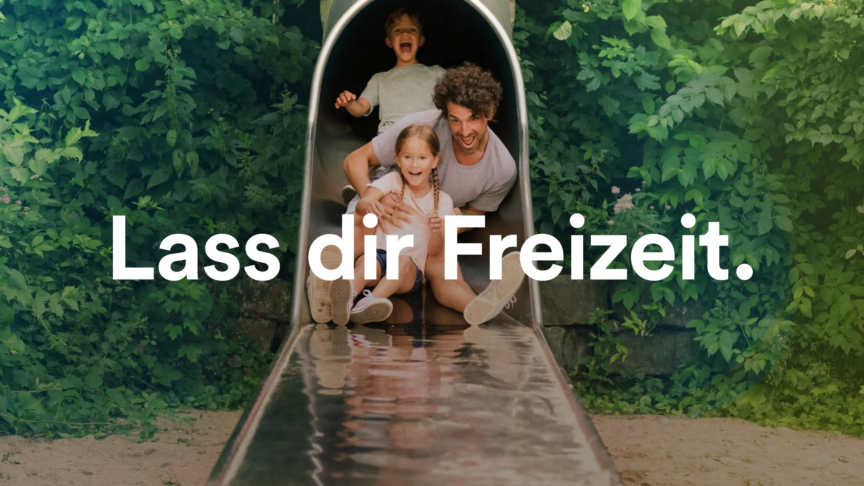 Erwachsener mit zwei Kindern auf einer Metallrutsche im Grünen, Text: 'Lass dir Freizeit'