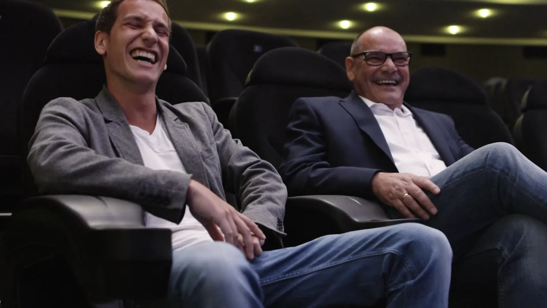 Zwei Männer sitzen lachend in einem Kinosaal