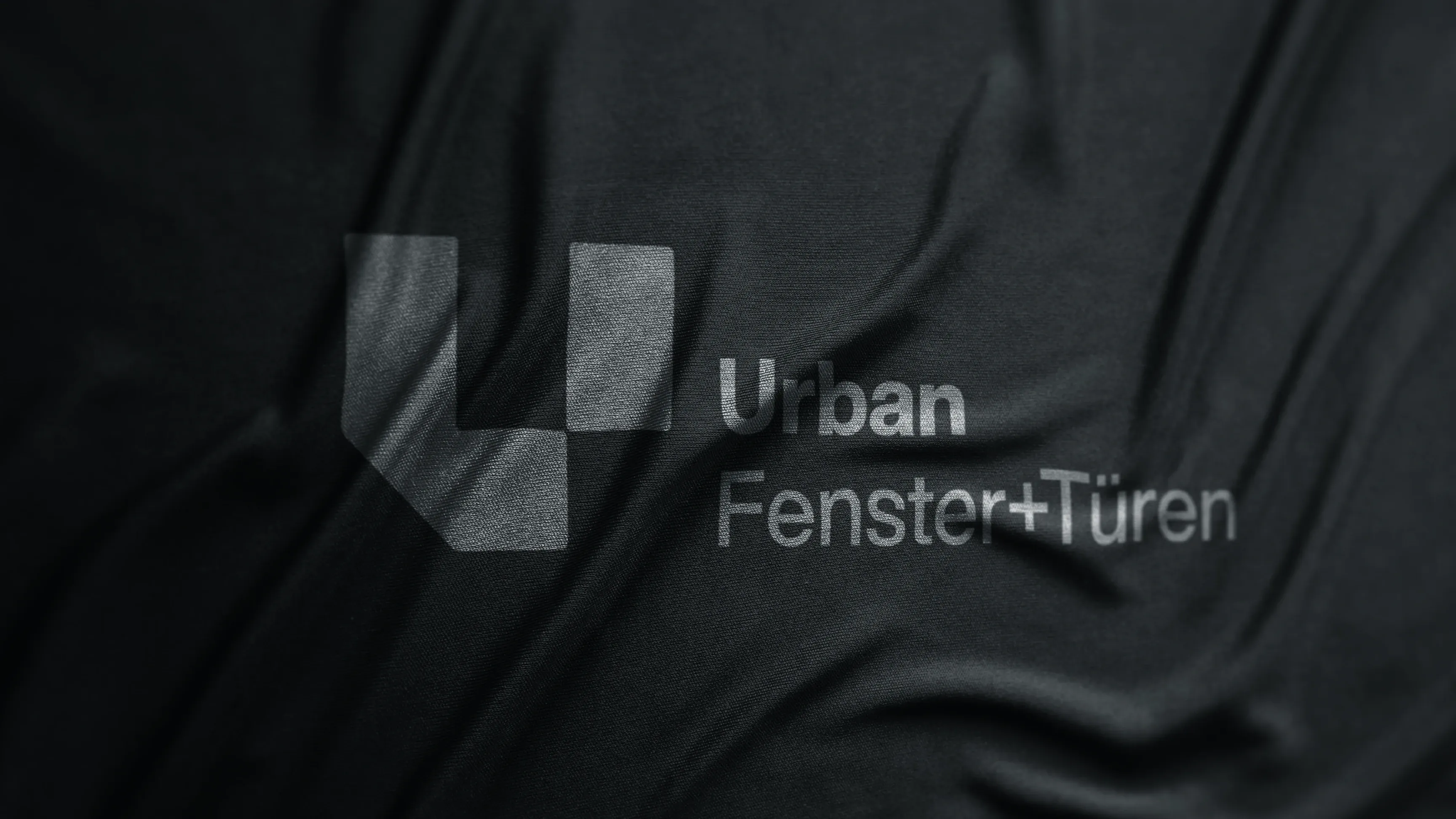 Logo Urban Fenster+Türen mit U-Symbol auf dunklem, zerknittertem Stoff