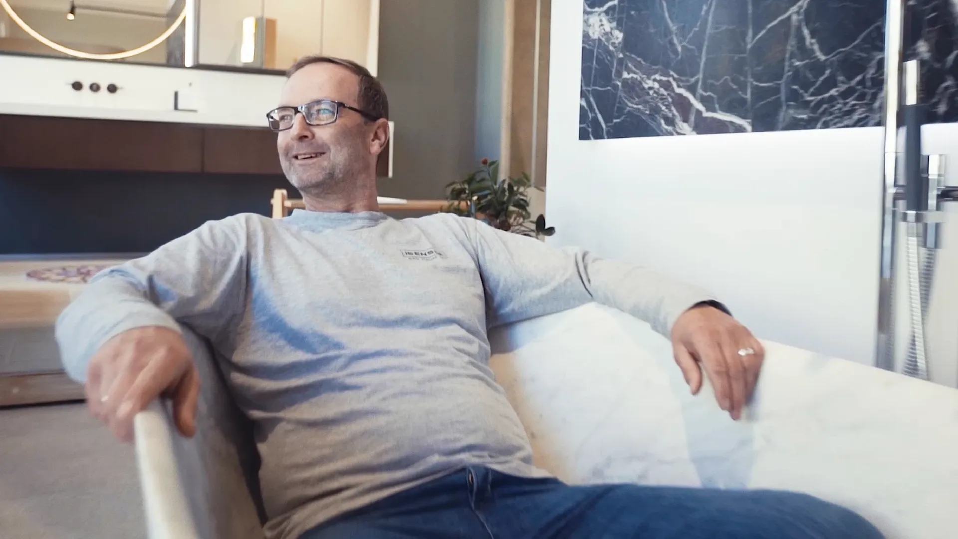 Mann mit Brille sitzt lächelnd in einer weißen Badewanne in modernem Badezimmer
