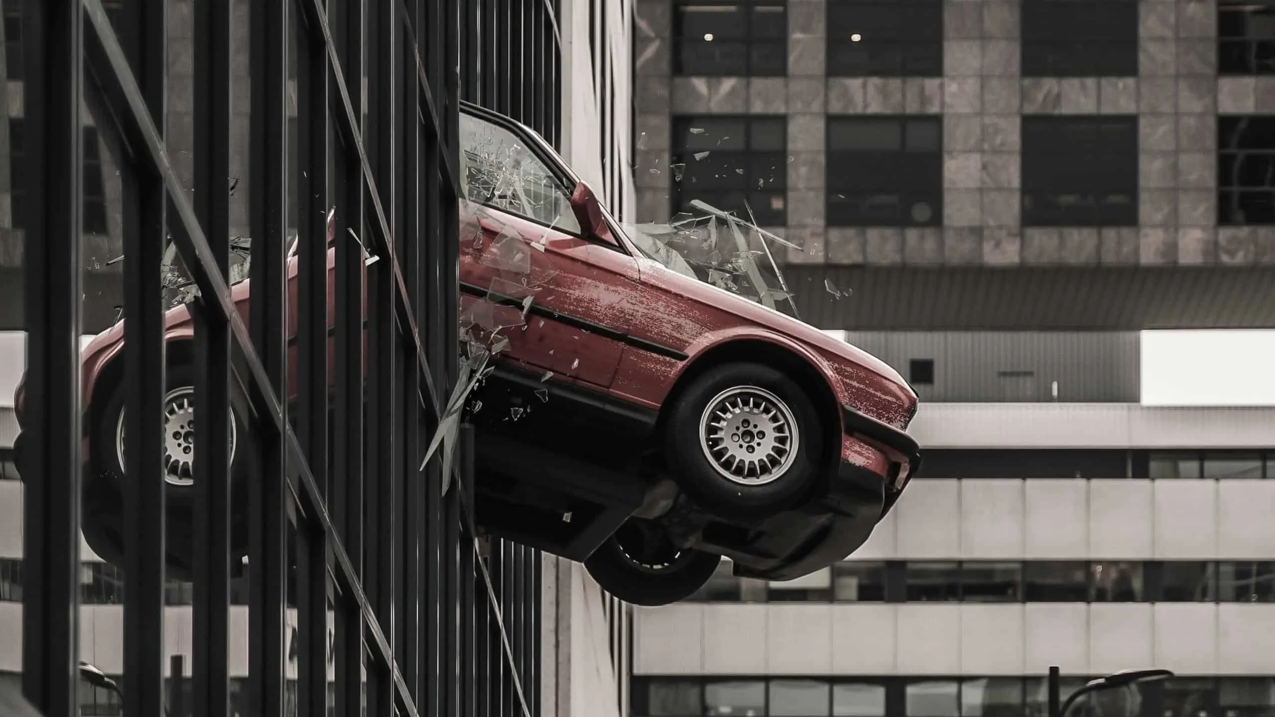 Rotes Auto durchbricht die Glasfassade eines Bürogebäudes