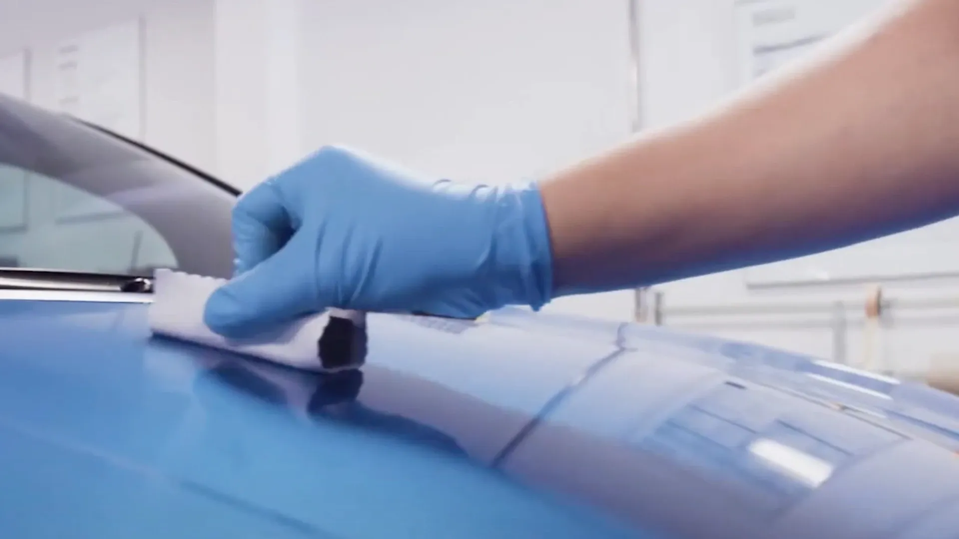 Hand mit blauen Handschuhen wischt die Motorhaube eines blauen Autos mit einem Tuch