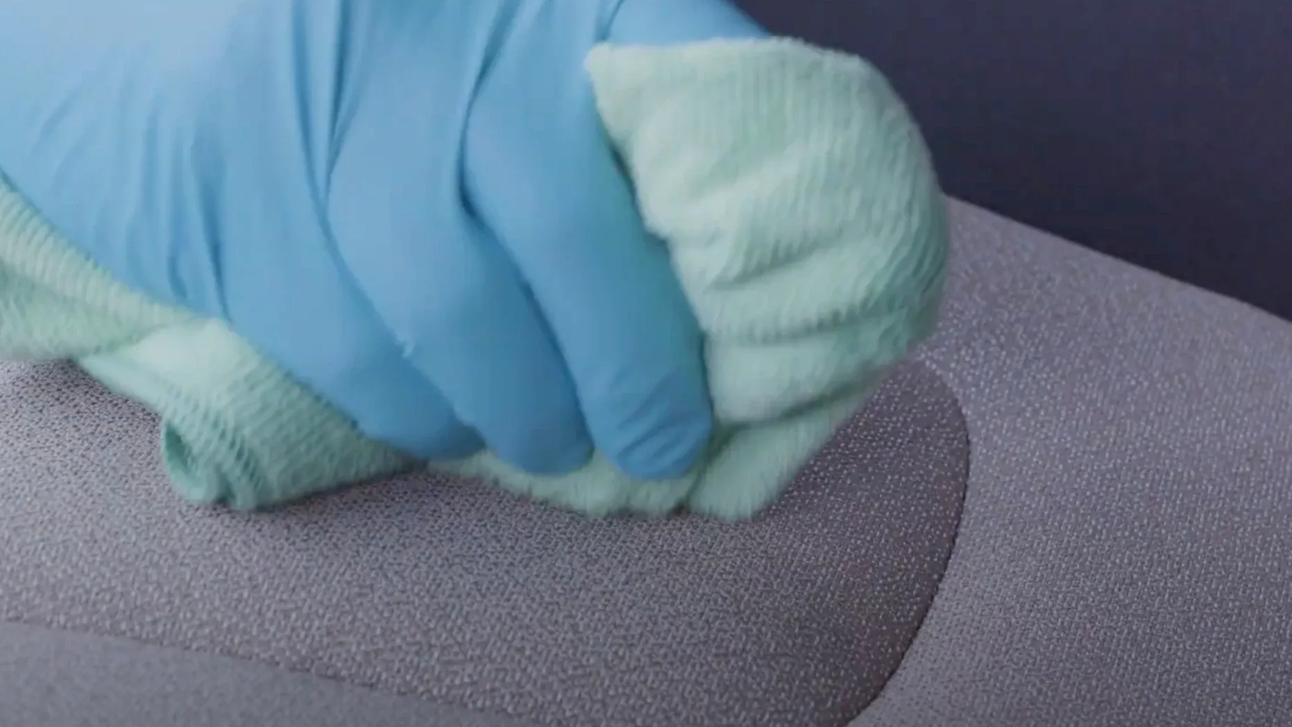 Behandschuhte Hand reinigt ein Stoffpolster mit einem Tuch