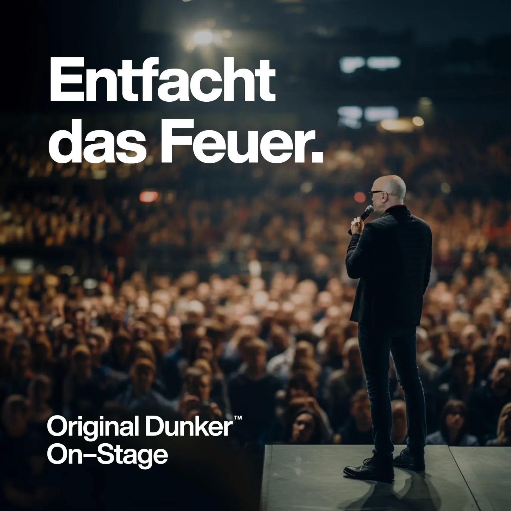 Redner mit Mikrofon auf Bühne vor großem Publikum, Text: 'Entfacht das Feuer' und 'Original Dunker On-Stage'